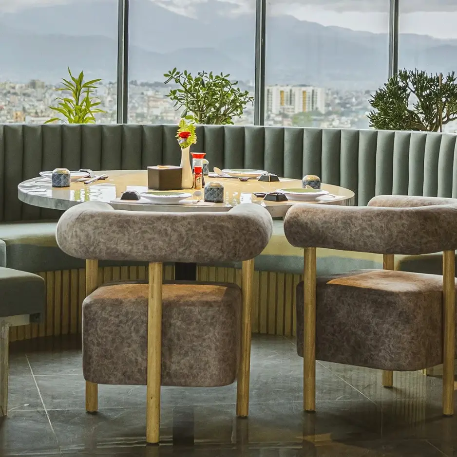 The rooftop dining room at Hokkaido Sora, with sage-green banquettes and floor-to-ceiling views over the Kathmandu valley at dusk.